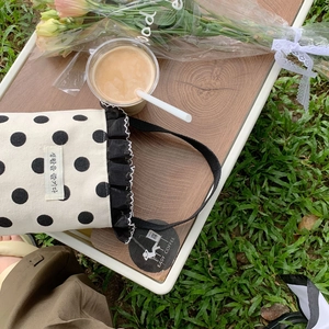 Close-up of beige canvas polka dot mini bag with black pleated lace on a picnic table