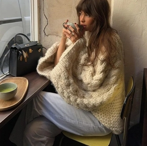 Detail of cream cable knit sweater with chunky texture and round neck in cozy cafe setting