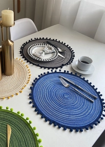Macro shot of circular woven placemat with pom-pom fringe edge and layered texture