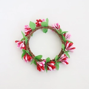 Macro detail of red and pink candle ring wreath with green leaves on rattan base