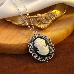 Macro shot of silver vintage cameo necklace with black oval pendant on wooden tray