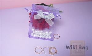 Detail of purple organza gift bag with silver bow, red rose, pearls and rose gold rings