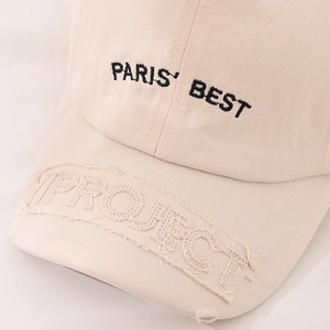 Detailed close-up of beige cotton baseball cap with PARIS BEST embroidery and frayed edges