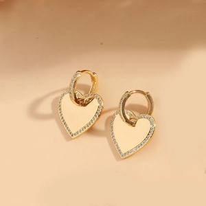 Gros plan de boucles d'oreilles cœur en or avec zircons micro-pavés sur fond beige
