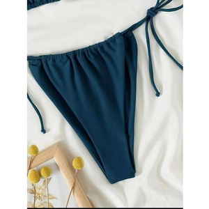 Detail of dark blue bikini bottom with side ties and ruching on white fabric