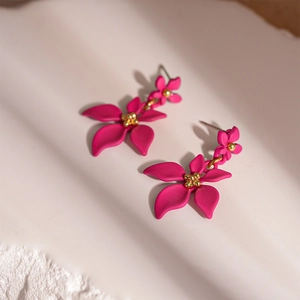 Gros plan de boucles d'oreilles fleurs rose mat avec perle dorée sur plateau texturé