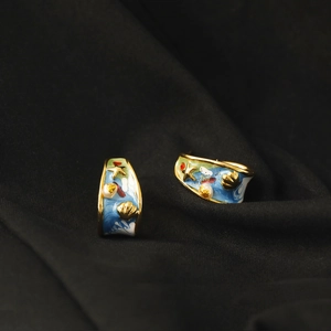 Macro shot of gold ocean-themed earrings with blue enamel, starfish, shell, and pearl details