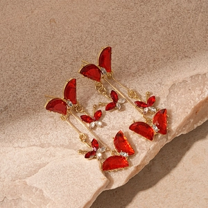 Detail of red butterfly tassel earrings with gold plating on a textured stone surface