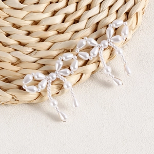 Detail view of handmade pearl bow earrings featuring intricate woven beadwork and tassels