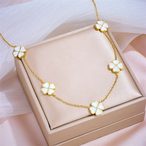 Gold chain necklace with five white clover pendants displayed on pink silk fabric