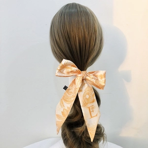 Orange silk hair scarf with tropical leaf print and letter E tied on a ponytail