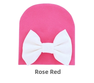 Close-up of rose red baby knit hat with a large white bow detail on plain background