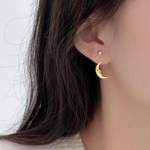 Close-up of golden moon stud earrings with embossed face details on model ear