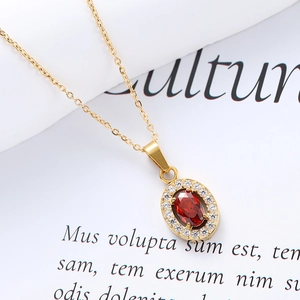 Close-up of a gold-plated oval pendant with a red gemstone and white zircon halo