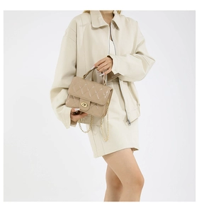 Chic beige quilted crossbody bag with a gold chain strap and turn-lock closure on a model