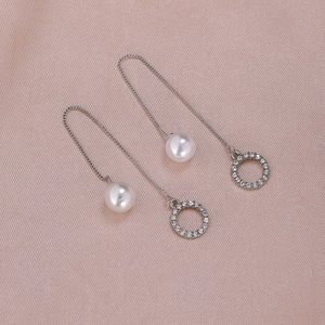 Close-up of elegant long pearl drop earrings with sparkling rhinestone rings on silk