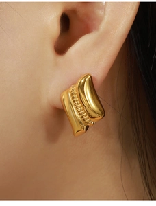 Close-up of geometric gold earrings featuring layered textures and beadwork on model