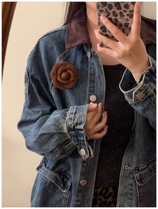 Detailed view of a brown velvet camellia flower brooch worn on a blue denim jacket