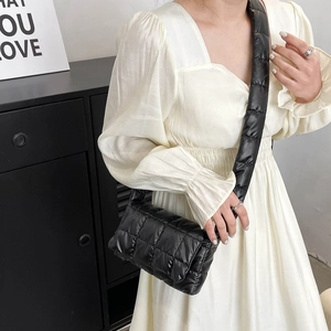 Close-up of a black quilted crossbody bag with a wide padded strap worn by a model