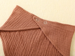 Close-up of muslin cotton baby bib texture and dual silver metal snap fasteners