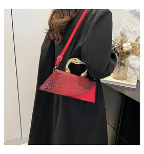 Detail of red croc-embossed handbag featuring a gold sculptural handle and shoulder strap