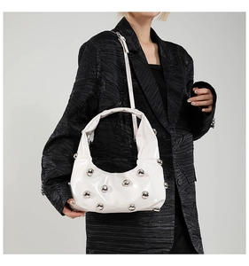 Close-up of white glossy shoulder bag featuring silver stud details on a black coat