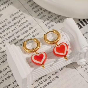 Détail rapproché de boucles d'oreilles créoles dorées avec breloques en cœur émaillé