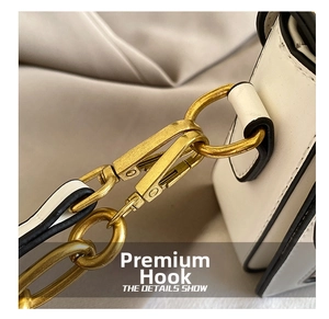 Detailed close-up of golden metal hook and hardware on a white leather handbag