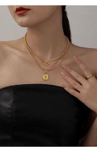 Detail of layered gold necklaces with queen coin pendant and OT buckle on model neck
