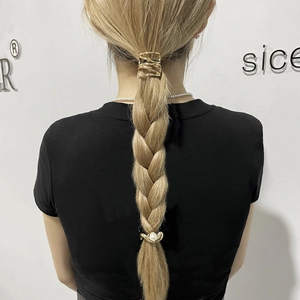 Detailed view of a golden geometric hair clip and pearl hair tie on a blonde braid