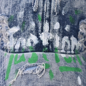 Detail of washed denim baseball cap with hand-painted graffiti and distressed rip effects