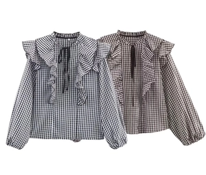 Close-up of V-neck ruffle collar and tie detail on checkered long sleeve shirt