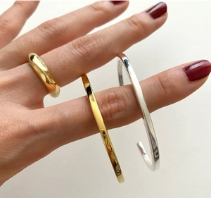 Close-up of minimalist gold and silver open bangles and a sleek ring on a model