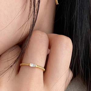 Dettaglio dell'anello dorato a treccia con zircone a taglio baguette sul dito
