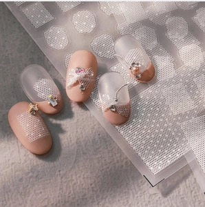 Macro shot of delicate white lace patterns and mesh nail stickers on manicured nails