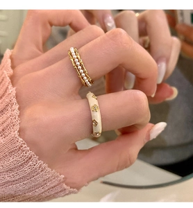 Detailed view of pearl bamboo ring and cream enamel star ring on female fingers