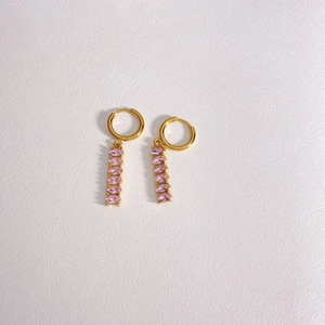 Detail of gold hoop earrings with cascading pink oval zircon tassels on white leather