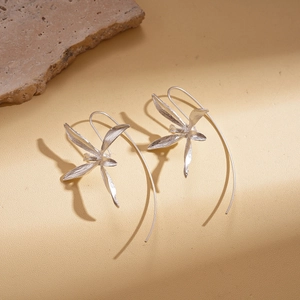 Detail of silver iris flower earrings with long hooks on a minimalist textured stone background
