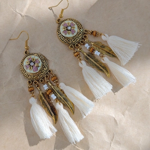 Macro detail of Bohemian tassel earrings with bronze leaves and white fringe texture