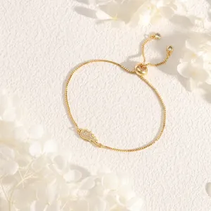 Detailed view of a gold wing pendant bracelet with cubic zirconia on a textured background