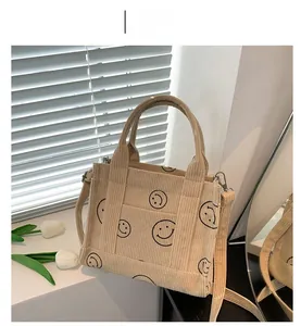 Close-up of off-white corduroy tote bag with black smiley faces and metal hook details