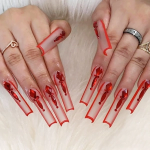 Extra long coffin false nails with red tips and rhinestone accents on white fur background