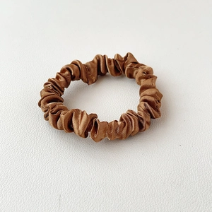 Detail van de gladde satijnen textuur en elegante plooien van de karamelbruine scrunchie
