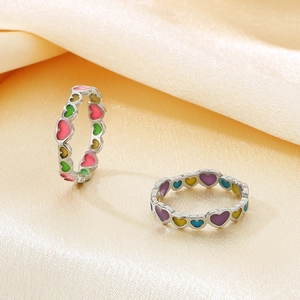 Detailed view of colorful enamel heart rings on an elegant silk fabric background