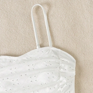 Detail of white swimsuit featuring elegant eyelet embroidery and thin shoulder straps