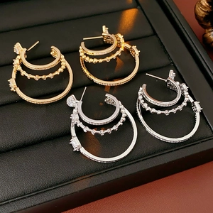 Macro shot of gold and silver triple-layered hoop earrings with inlaid zircons on black tray