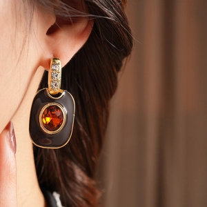 Detail of vintage gold-tone earrings with black enamel and amber gemstone on a model