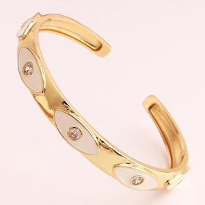 Detailed view of gold C-shaped cuff bracelet with white enamel evil eye and inlaid crystals