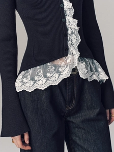 Detail of white floral lace trim and textured knit on a black French style cardigan
