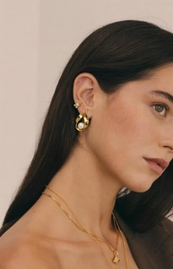 Close-up of a gold U-shaped earring featuring a large white pearl on a model's ear